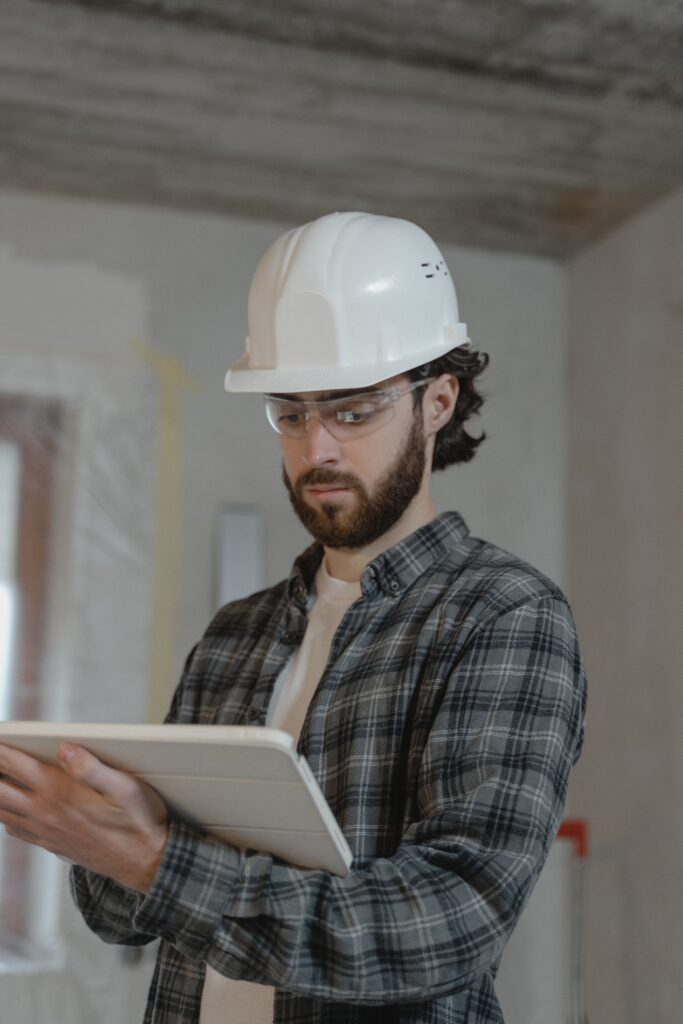 pexels-photo-6474492-6474492 Male construction engineer assessing building plans indoors, wearing a hard hat.